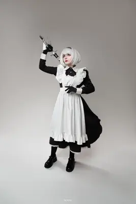 A cosplayer dressed as 2B from NieR: Automata, wearing a white and black gothic-lolita dress with a sword in hand.