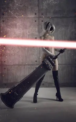 A cosplayer portrays 2B from NieR: Automata, standing with a large sword in a post-apocalyptic setting.
