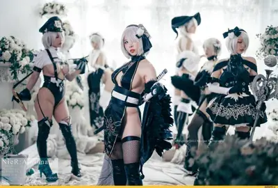 Three cosplayers dressed as 2B and A2 from NieR:Automata pose outdoors.