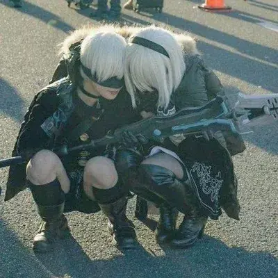 Cosplayers dressed as 2B and 9S from Nier Automata in a detailed outdoor convention setting